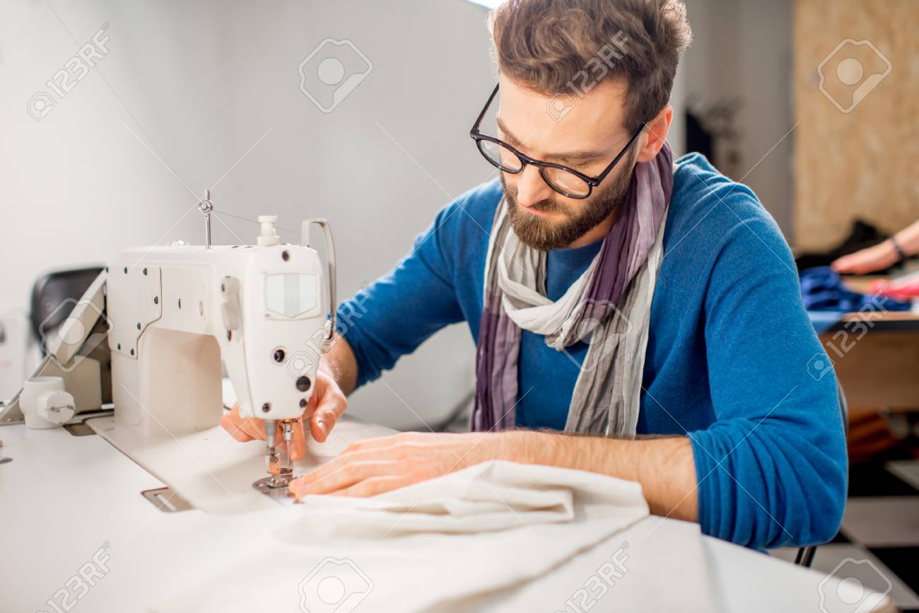 Handsome tailor sewing fabric with a sewing machine at the studio - 92357368 Handsome tailor sewing fabric with a sewing machine at the studio - 92357368