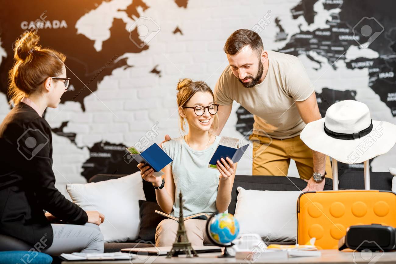 Young lovely couple sitting with manager at the travel agency office prepairing for a summer vacation - 92670479 Young lovely couple sitting with manager at the travel agency office prepairing for a summer vacation - 92670479