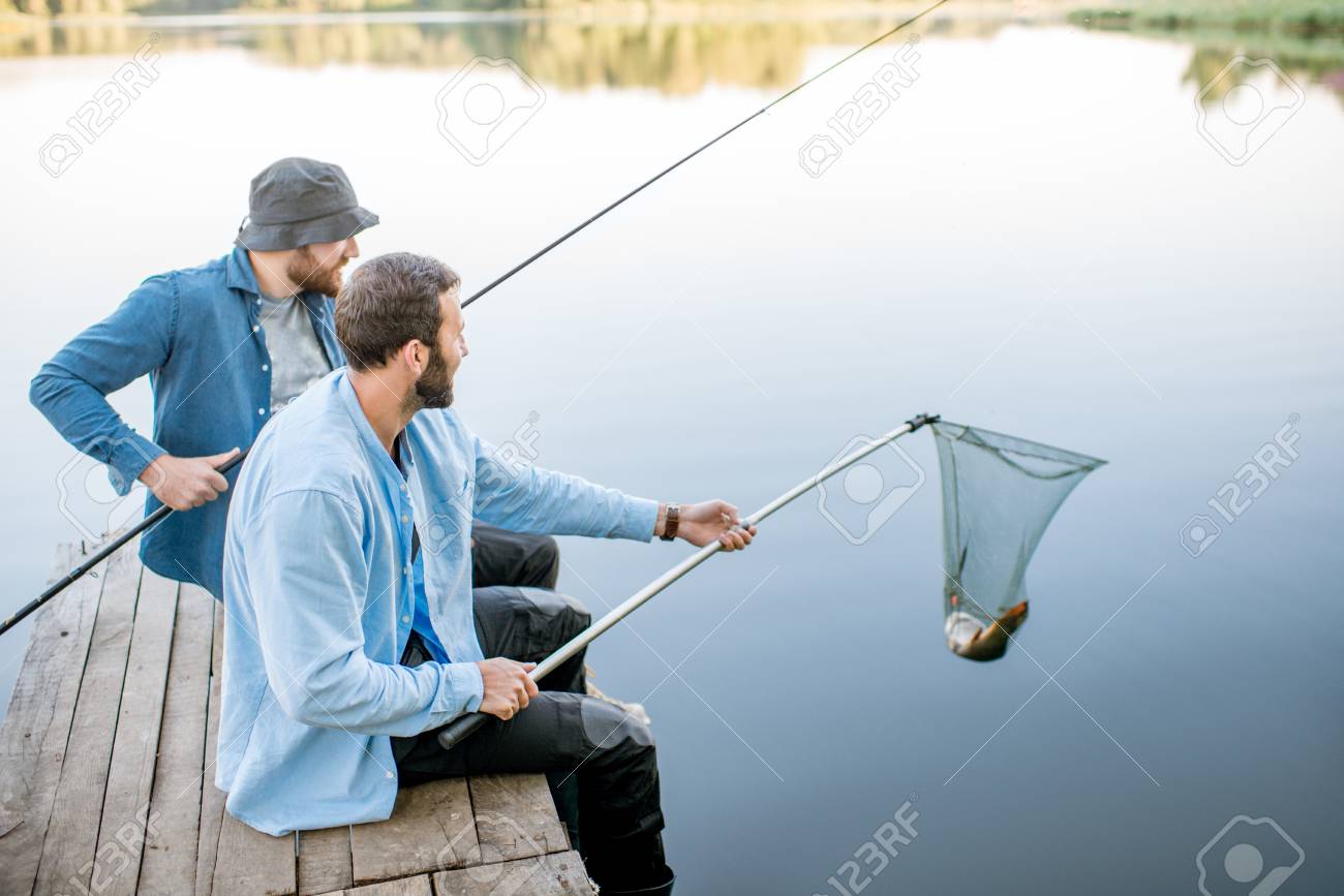 Two Friends Catching Fish With Fishing Net And Rod Sitting On