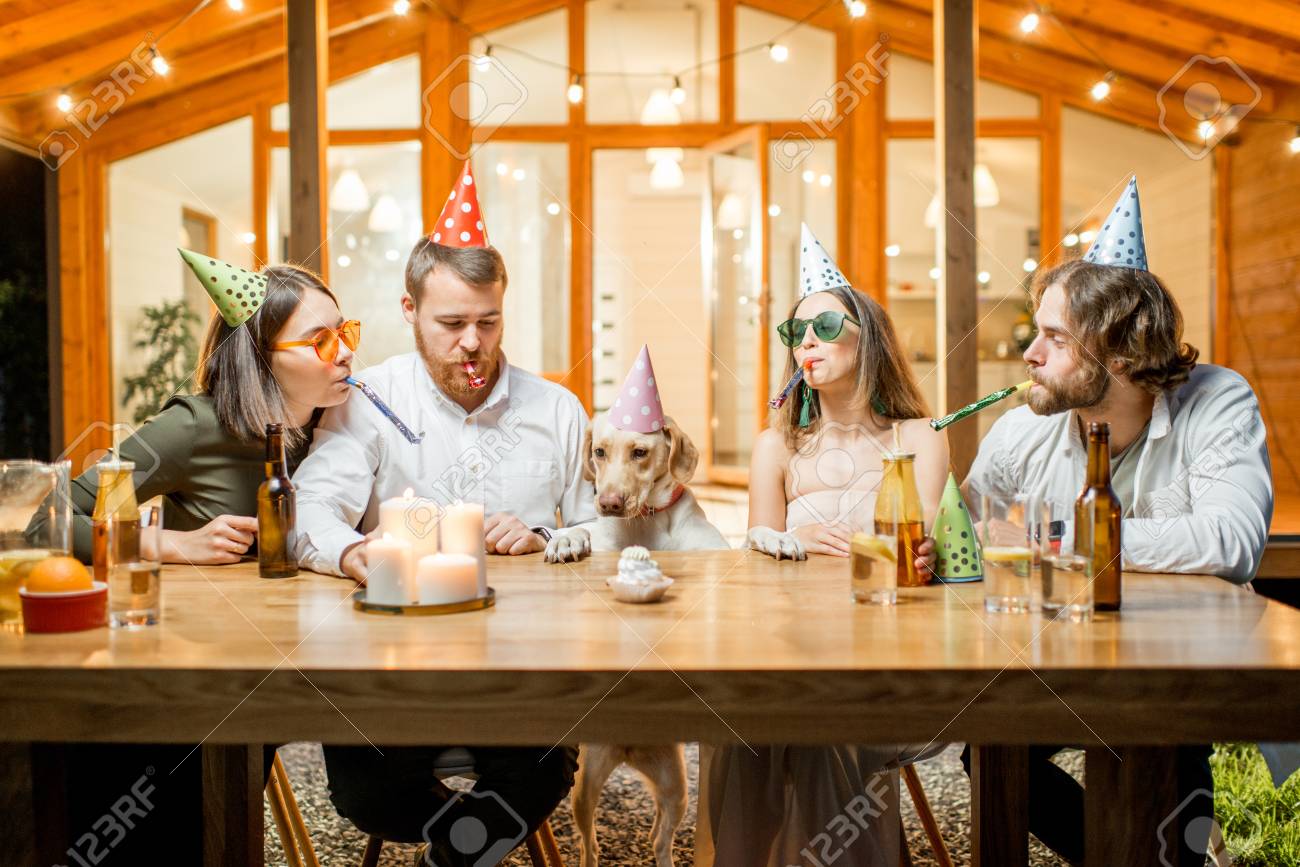 Friends celebrating dogs birthday with cake at the table on the backyard of the house in the evening - 105233922 Friends celebrating dogs birthday with cake at the table on the backyard of the house in the evening - 105233922