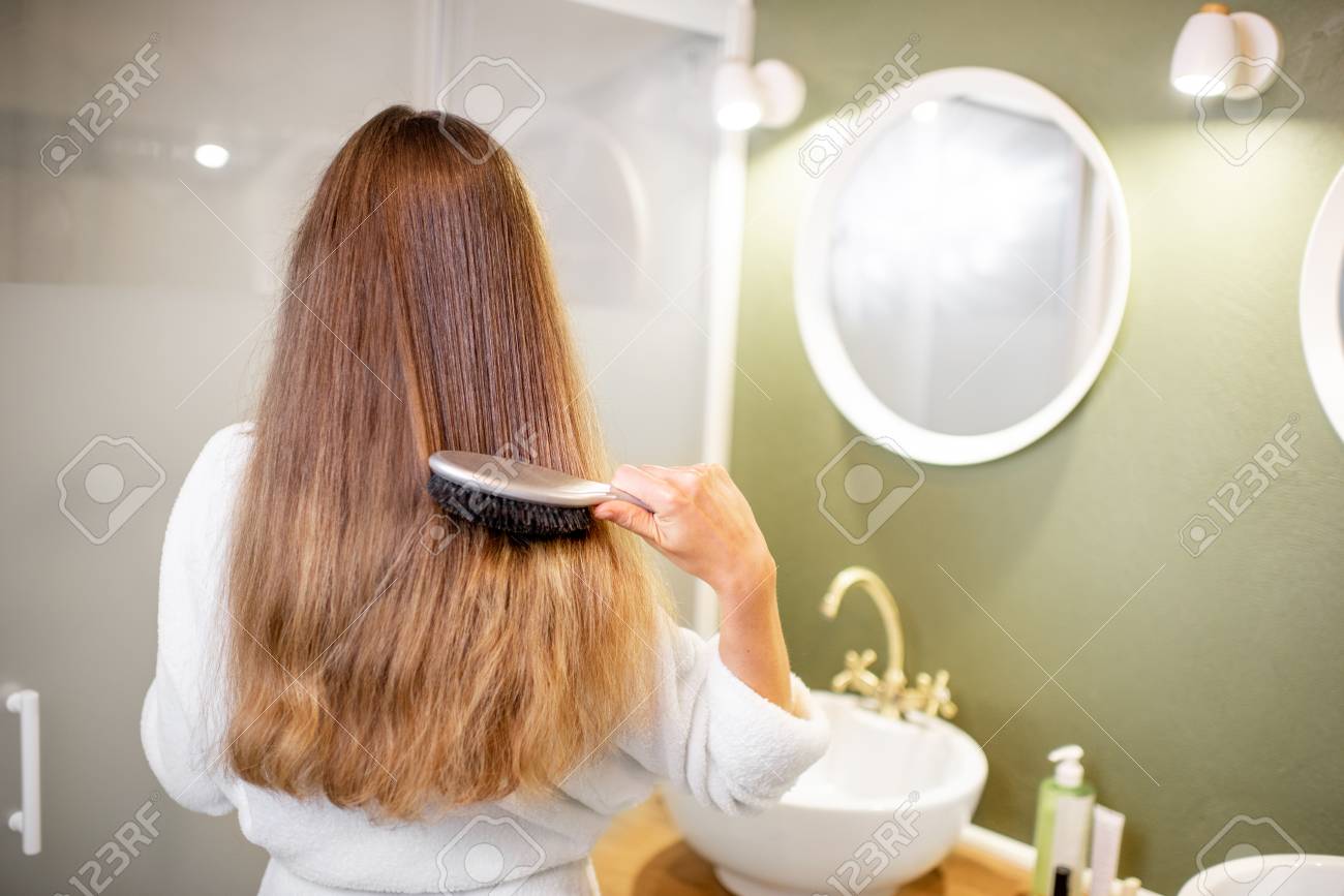 Woman in bathrobe combing hair with brush in the bathroom, rear view - 113338199 Woman in bathrobe combing hair with brush in the bathroom, rear view - 113338199