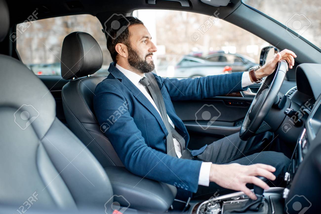 Handsome bearded businessman dressed in the suit driving a car in the city - 112372574 Handsome bearded businessman dressed in the suit driving a car in the city - 112372574