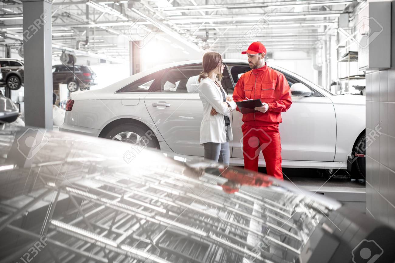 Young woman client with auto mechanic in red uniform at the car service. Wide angle view with copy space - 113406163 Young woman client with auto mechanic in red uniform at the car service. Wide angle view with copy space - 113406163