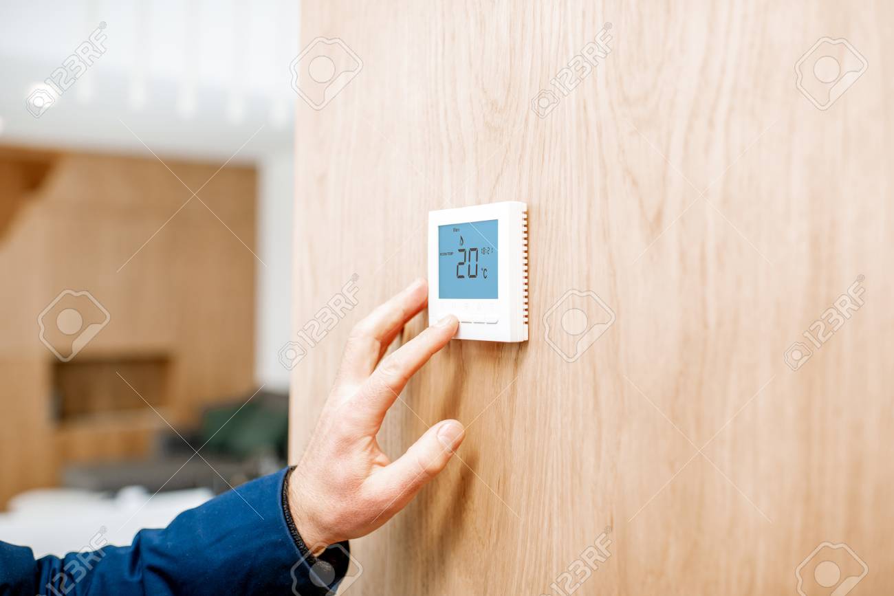 Adjusting room temperature with electronic thermostat at home, close-up view with no face - 114136211 Adjusting room temperature with electronic thermostat at home, close-up view with no face - 114136211