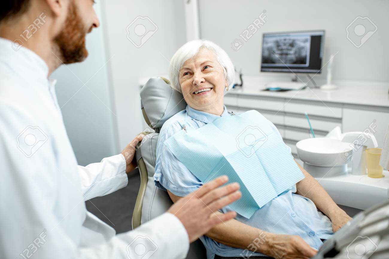 Beautiful elder woman with healthy smile sitting during the consultation with dentist at the dental office - 114781068 Beautiful elder woman with healthy smile sitting during the consultation with dentist at the dental office - 114781068