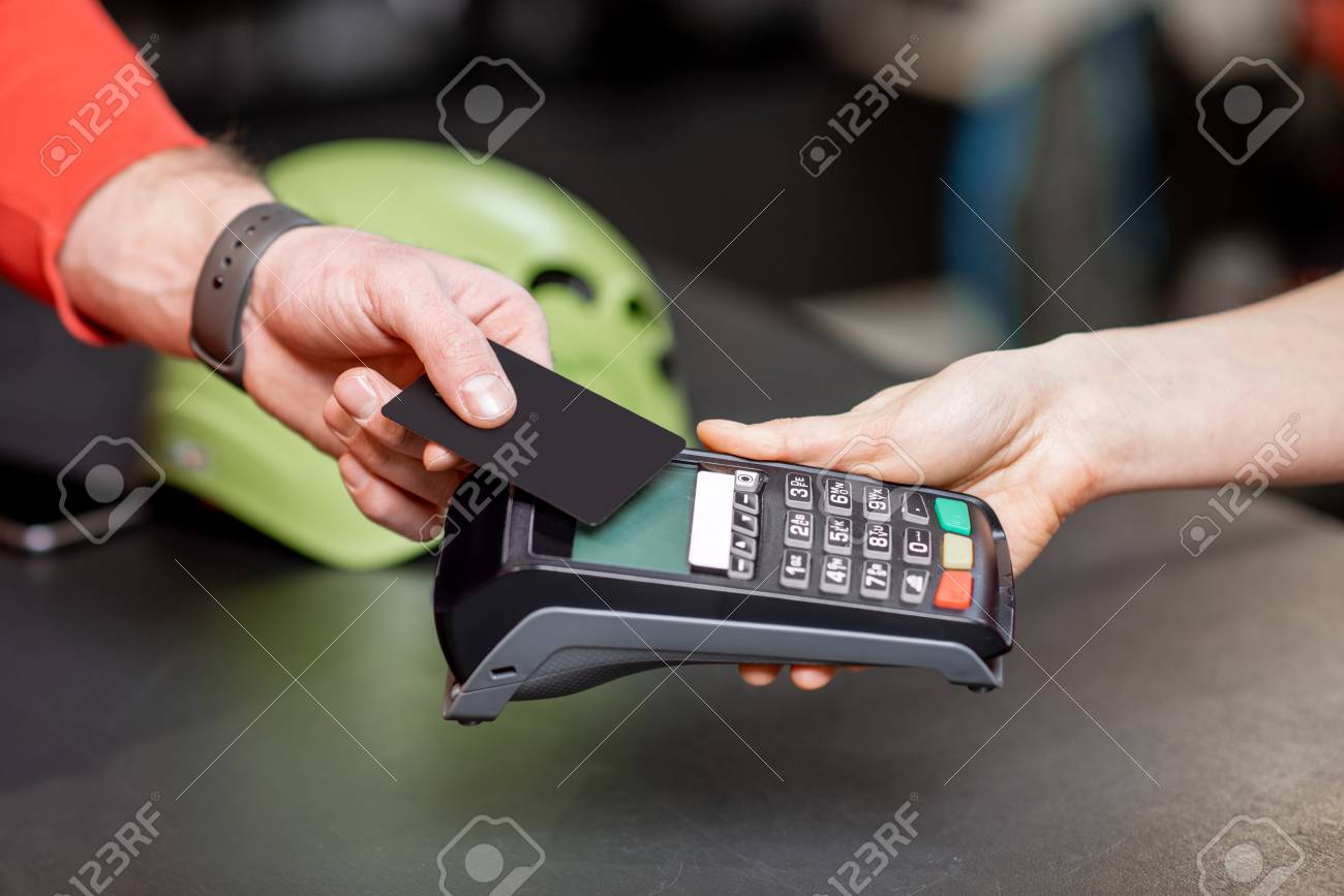 Man making purchase with bank card and cash register at the counter of the sports shop, close-up view - 115281473 Man making purchase with bank card and cash register at the counter of the sports shop, close-up view - 115281473