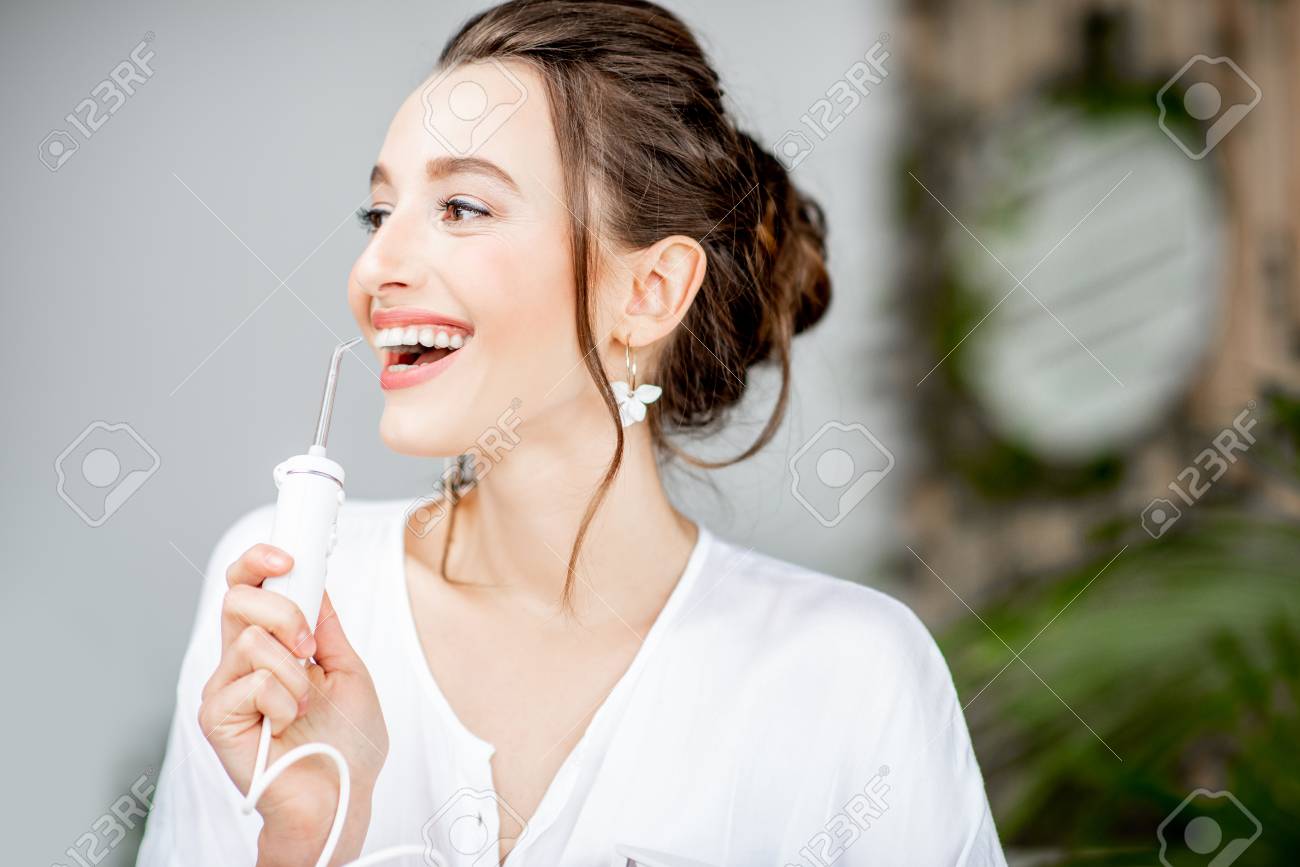 Portrait of a beautiful woman with shiny smile holding irrigator tool for teeth cleaning in the bathroom - 116442289 Portrait of a beautiful woman with shiny smile holding irrigator tool for teeth cleaning in the bathroom - 116442289