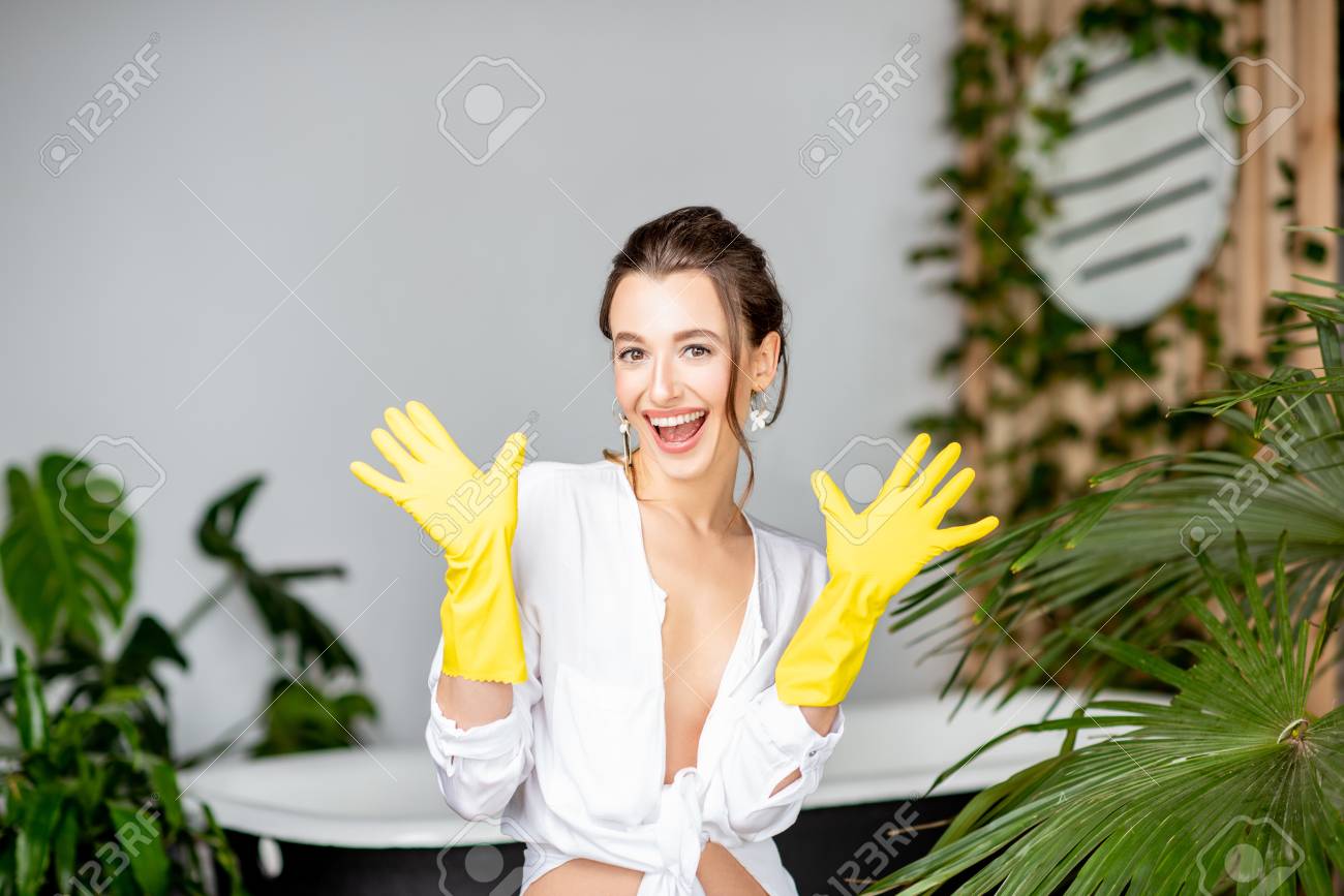 Portrait of a young and cheerful woman wearing yellow protective gloves as a housewife in the bathrrom - 116443019 Portrait of a young and cheerful woman wearing yellow protective gloves as a housewife in the bathrrom - 116443019