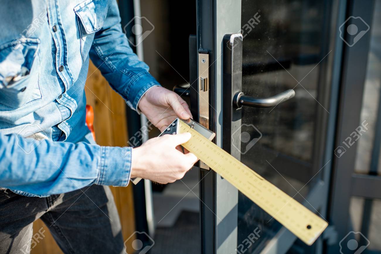 Man changing core of a door lock of the entrance glass door, close-up view with no face - 118140082 Man changing core of a door lock of the entrance glass door, close-up view with no face - 118140082
