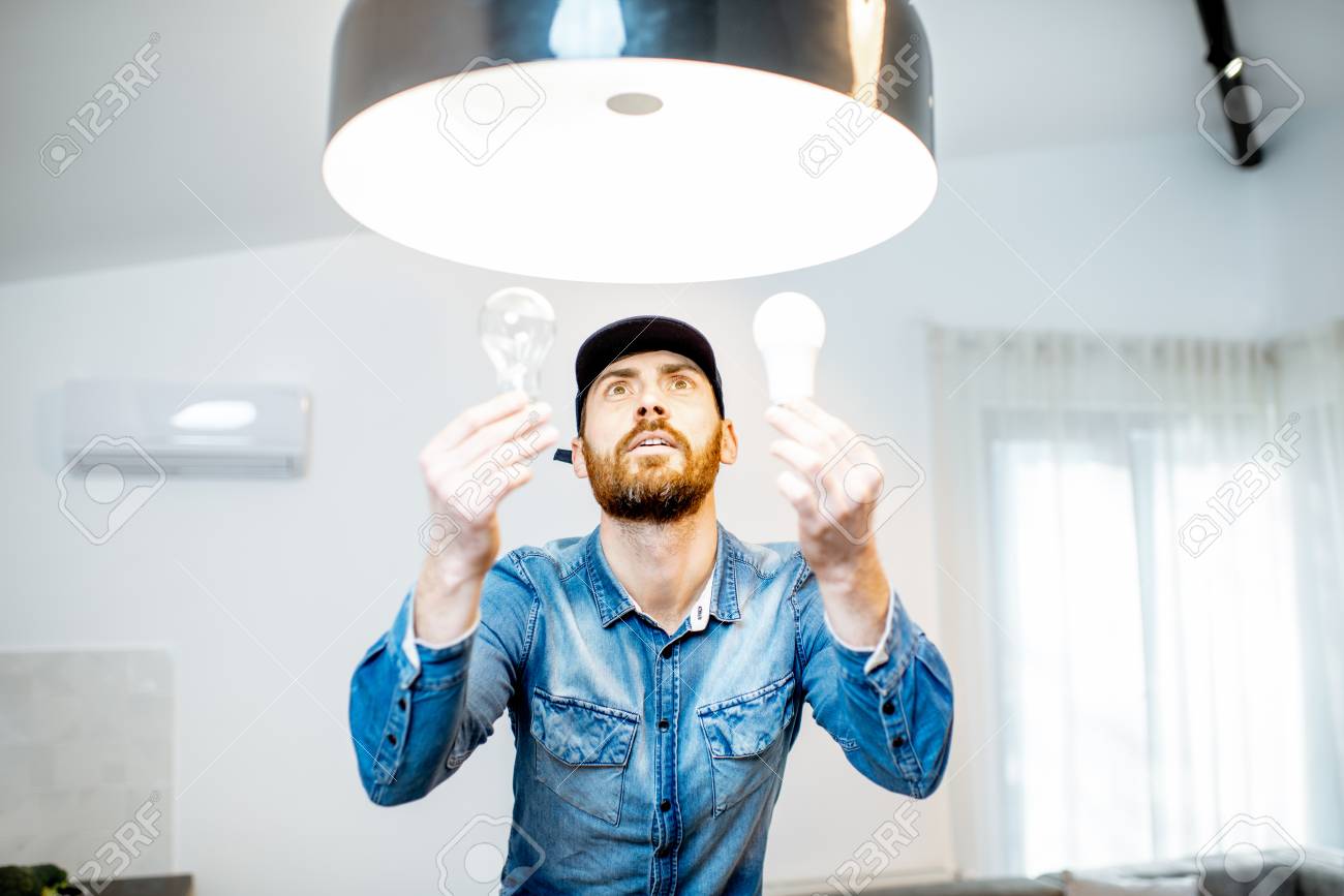 Handyman choosing between energy save and cheap incandescent lamp while changing light in the appartment - 118140142 Handyman choosing between energy save and cheap incandescent lamp while changing light in the appartment - 118140142