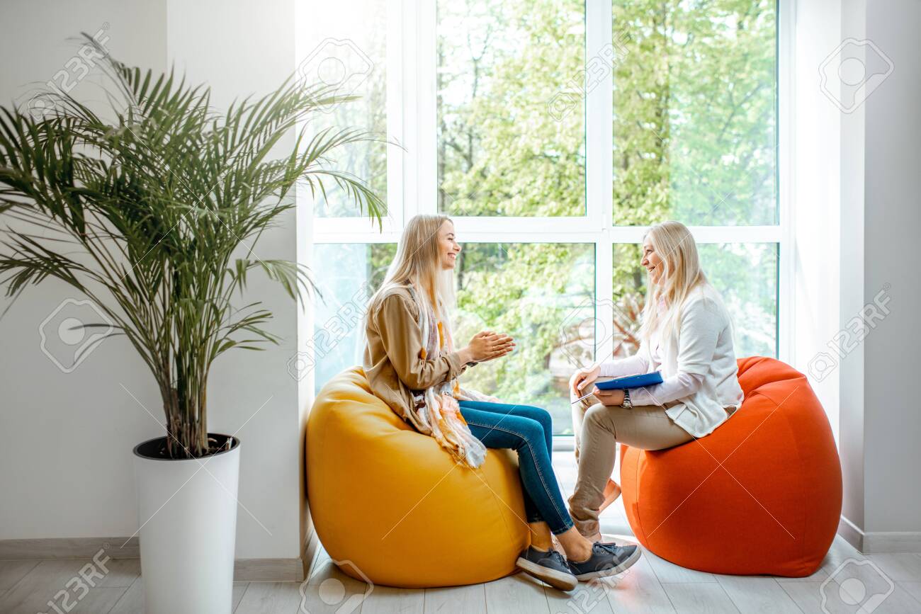 Young woman with senior female psychologist or mental coach sitting on the comfortable chairs during the psychological counseling in the office - 122230245 Young woman with senior female psychologist or mental coach sitting on the comfortable chairs during the psychological counseling in the office - 122230245