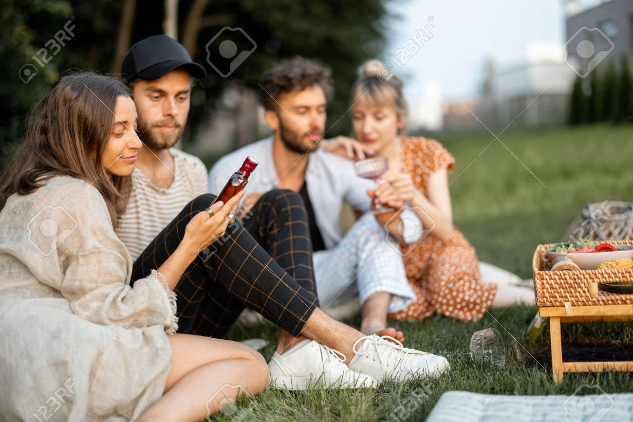 Young friends sit together and hug, talk and drink alcohol in a close and friendly atmosphere on a picnic in the evening - 172037521 Young friends sit together and hug, talk and drink alcohol in a close and friendly atmosphere on a picnic in the evening - 172037521