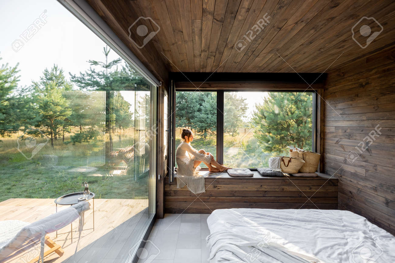 Young woman resting at beautiful country house or hotel, sitting on the window sill enjoying beautiful view on pine forest. Concept of solitude and recreation on nature - 172224119 Young woman resting at beautiful country house or hotel, sitting on the window sill enjoying beautiful view on pine forest. Concept of solitude and recreation on nature - 172224119