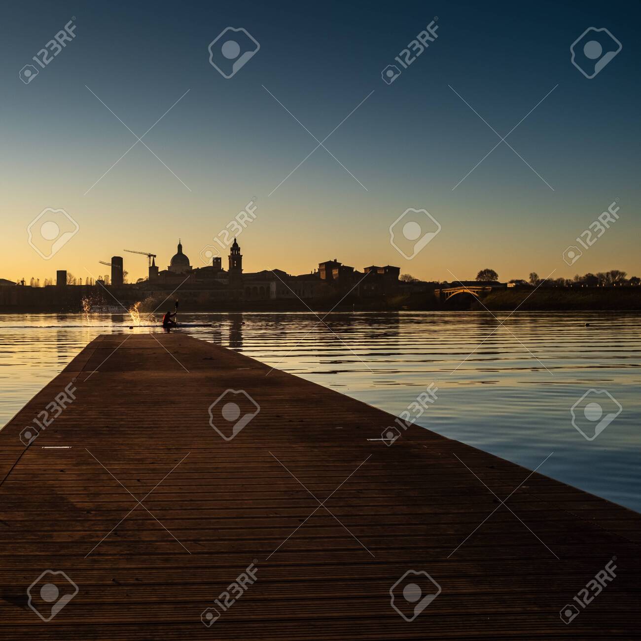 Adult male kayaker splashing water with paddle while kayaking on the Lago Inferiore (Inferior Lake) in front of the suggestive medieval profile of the Old Town of Mantua (Lombardy,Italy). - 138447488 Adult male kayaker splashing water with paddle while kayaking on the Lago Inferiore (Inferior Lake) in front of the suggestive medieval profile of the Old Town of Mantua (Lombardy,Italy). - 138447488