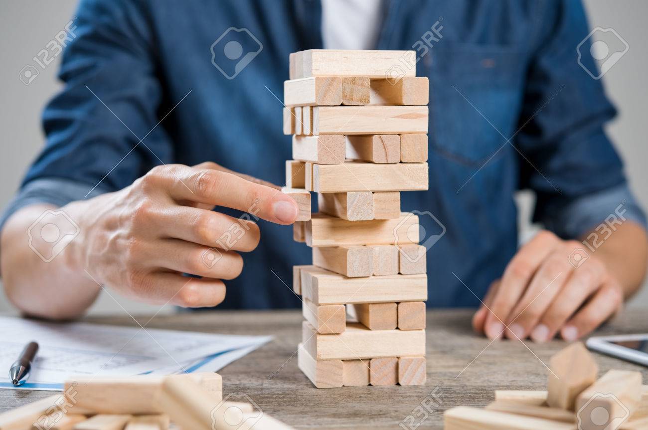 Businessman thinking about new challenge. Close up of hand of man taking a piece of building wooden bricks. Businessman trying to find a solution to problem by building with wooden bricks. Risk and strategy concept. - 64821171 Businessman thinking about new challenge. Close up of hand of man taking a piece of building wooden bricks. Businessman trying to find a solution to problem by building with wooden bricks. Risk and strategy concept. - 64821171