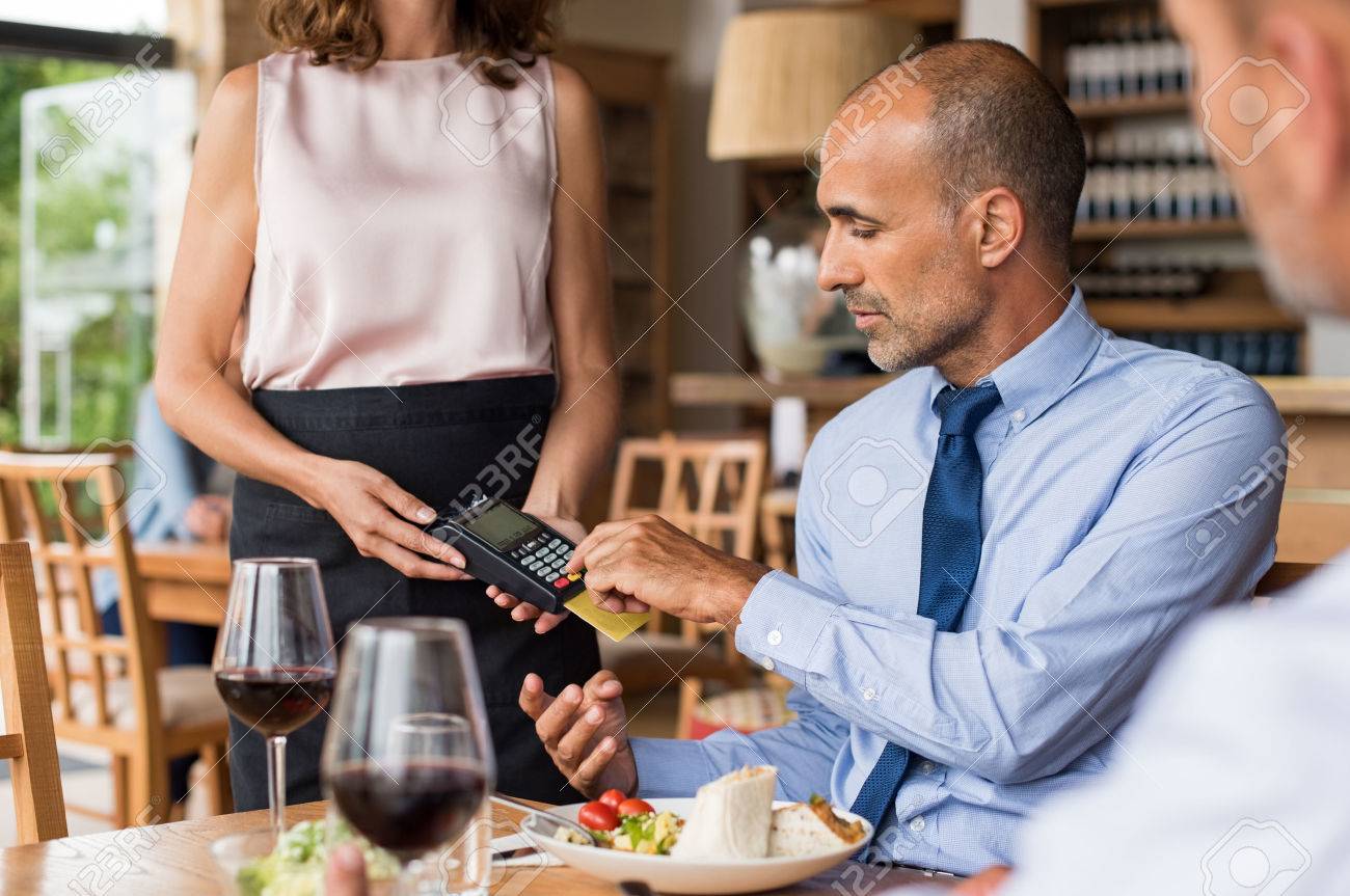 Waiter holding credit card swipe machine while customer typing code. Mature businessman making payment in cafe through credit card. Customer paying bill of lunch with debit card. - 75298833 Waiter holding credit card swipe machine while customer typing code. Mature businessman making payment in cafe through credit card. Customer paying bill of lunch with debit card. - 75298833