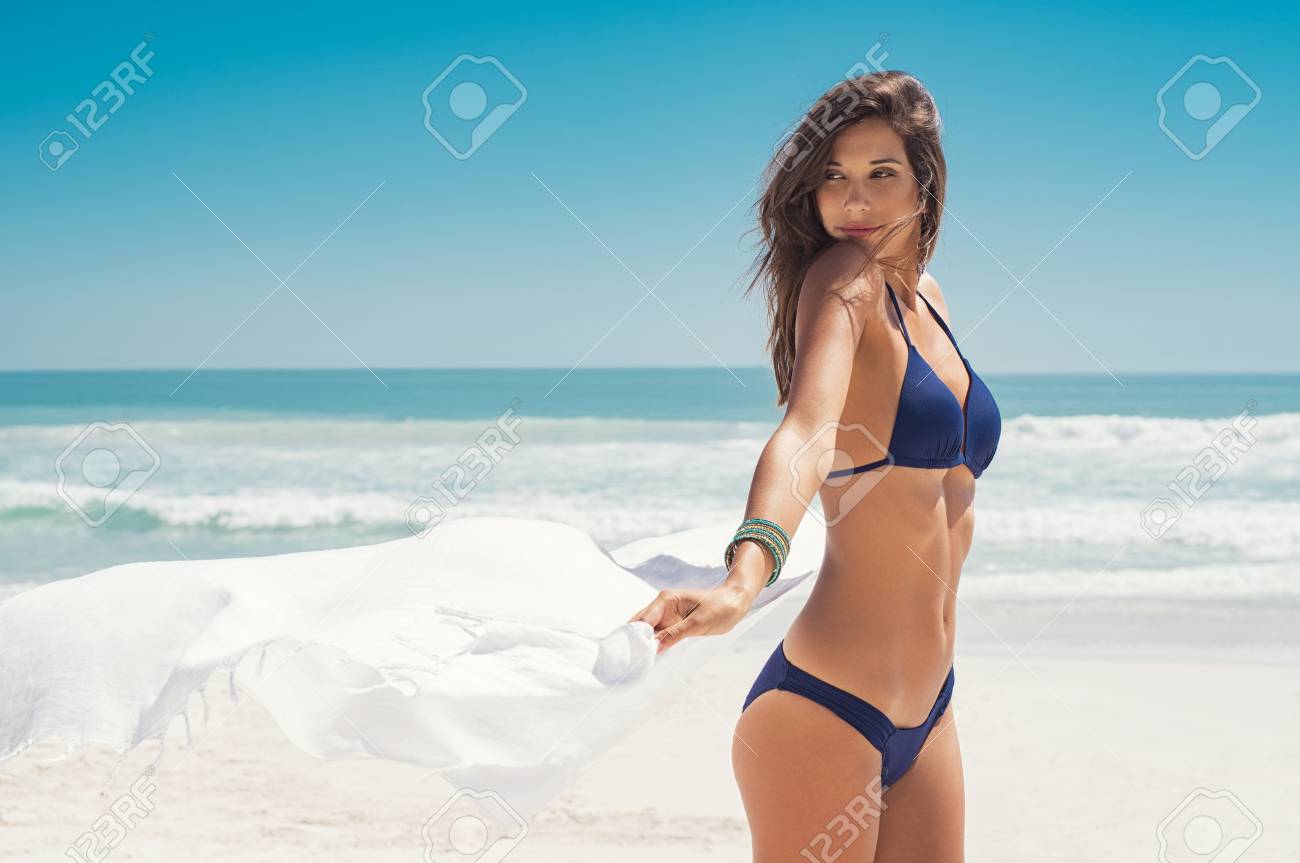 Young woman waving white scarf in wind at beach. Latin happy girl in blue bikini holding tissue and looking away at sea. Sexy fashion woman playing with the scarf on seashore. - 97278163 Young woman waving white scarf in wind at beach. Latin happy girl in blue bikini holding tissue and looking away at sea. Sexy fashion woman playing with the scarf on seashore. - 97278163