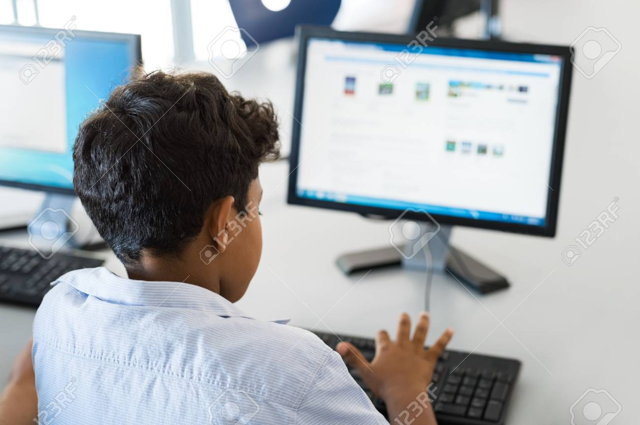 Rear View Of Multiethnic Boy Using Desktop Computer In School Library Back View Of Mixed Race Child Working In Classroom With Computer At Elementary School Young Arab Schoolboy Typing On Keyboard Stock
