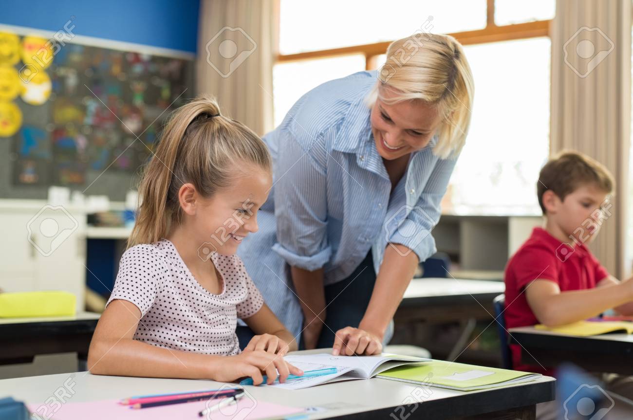 teacher and girls Happy Teacher Helping Young Girl With Study In Classroom. Teacher Teaching  To Smiling Schoolgirl At Elementary School. Diligent Child Sitting At  School Desk With Tutor. Stock Photo, Picture and Royalty Free Image.