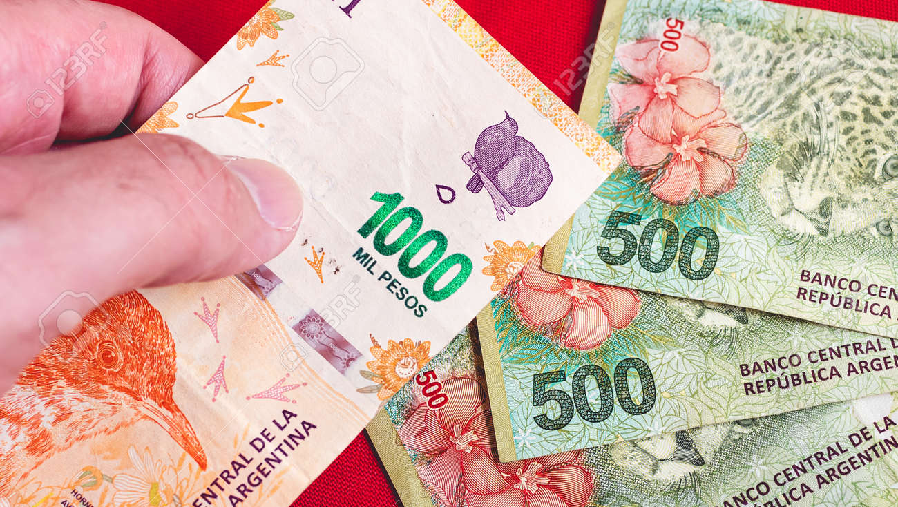 アルゼンチンの通貨であるアルゼンチンペソの1000ペソ紙幣を持ち、他の紙幣を背景に持っている人。経済と金融を表現するための写真。の写真素材・画像素材  Image 164114188
