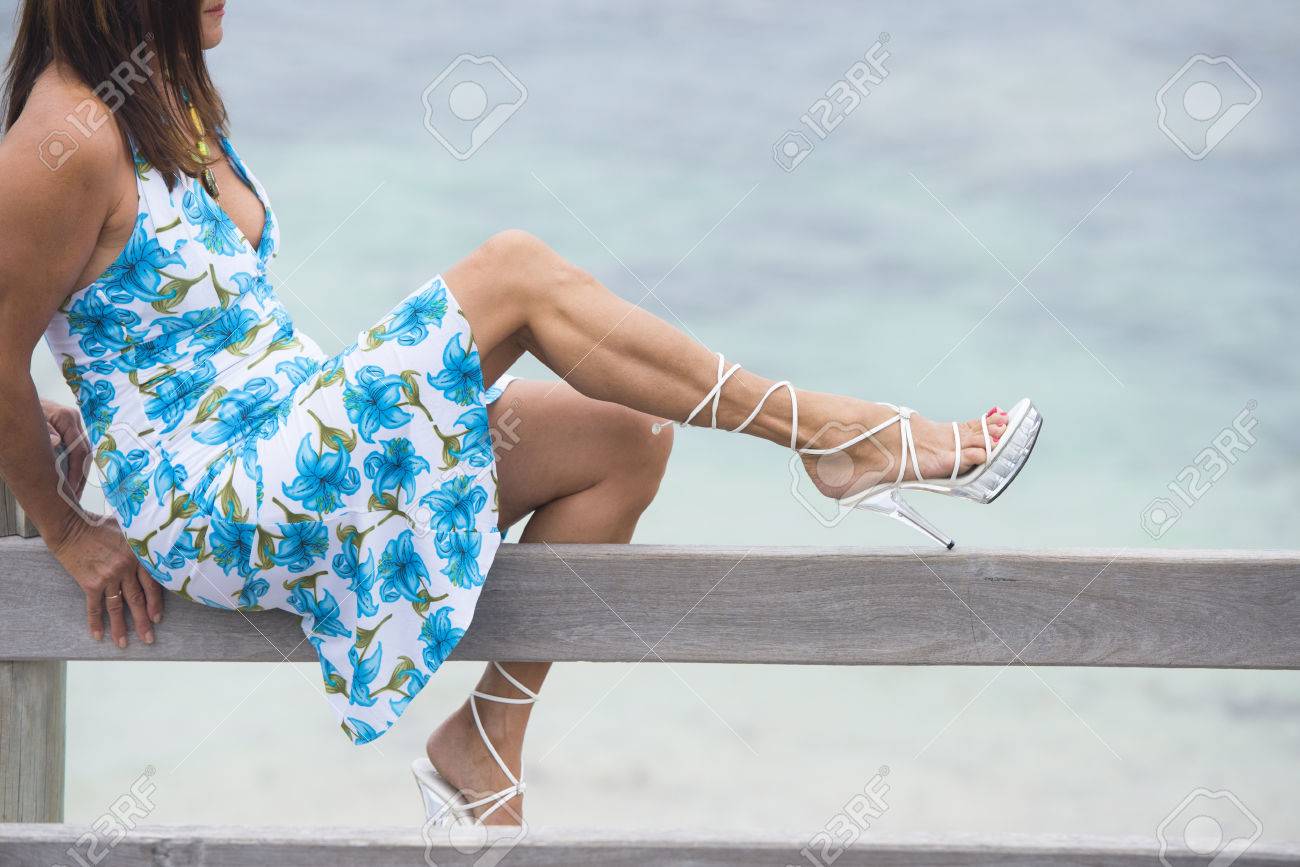 Portrait Attractive Mature Woman Sitting On Wooden Handrail Portrait attractive mature woman sitting on wooden handrail, wearing summer dress and high heel shoes - Portrait Attractive Mature Woman Sitting On Wooden Handrail