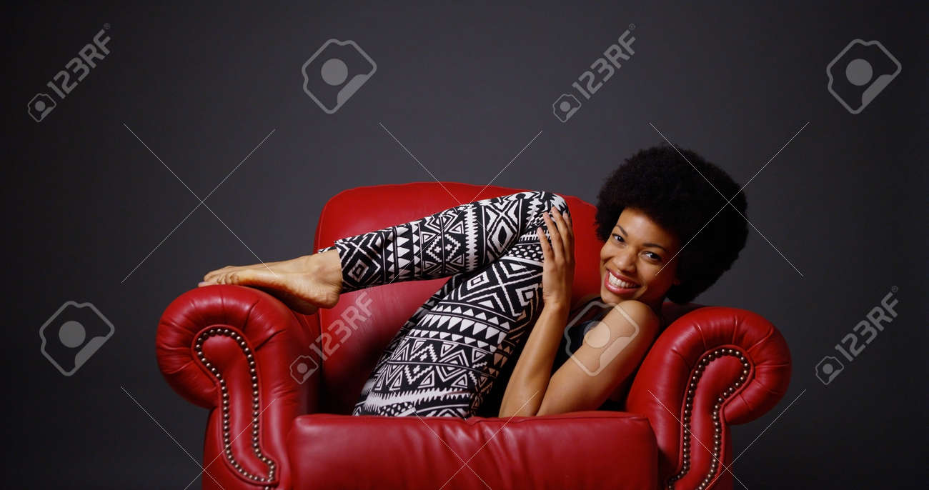 ふざけて足を蹴る赤い革の腕椅子にアフリカ女性 の写真素材 画像素材 Image