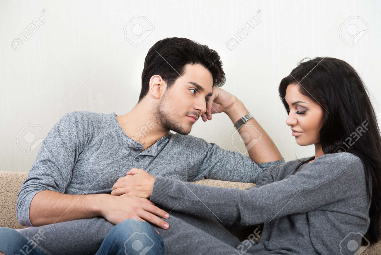 young happy couple talking each other sitting on a sofa stock photo