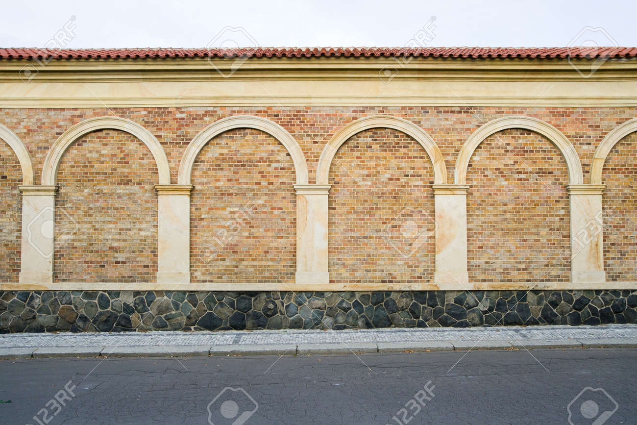 Classic decorative brick wall with columns, arches and stone base next to the sidewalk and street - 9292029 Classic decorative brick wall with columns, arches and stone base next to the sidewalk and street - 9292029