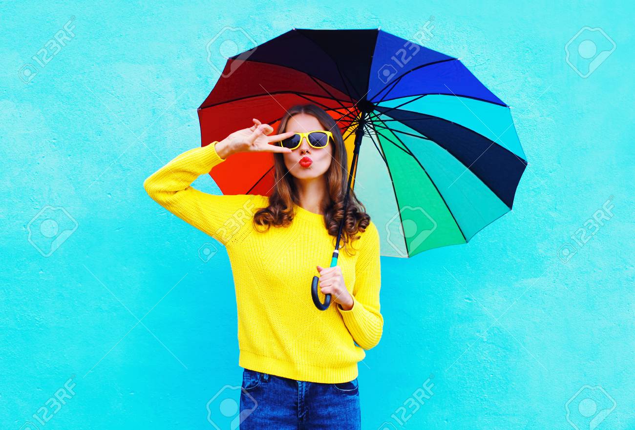 Fashion pretty cool woman holding colorful umbrella in autumn day over blue background wearing a yellow knitted sweater - 63469295 Fashion pretty cool woman holding colorful umbrella in autumn day over blue background wearing a yellow knitted sweater - 63469295