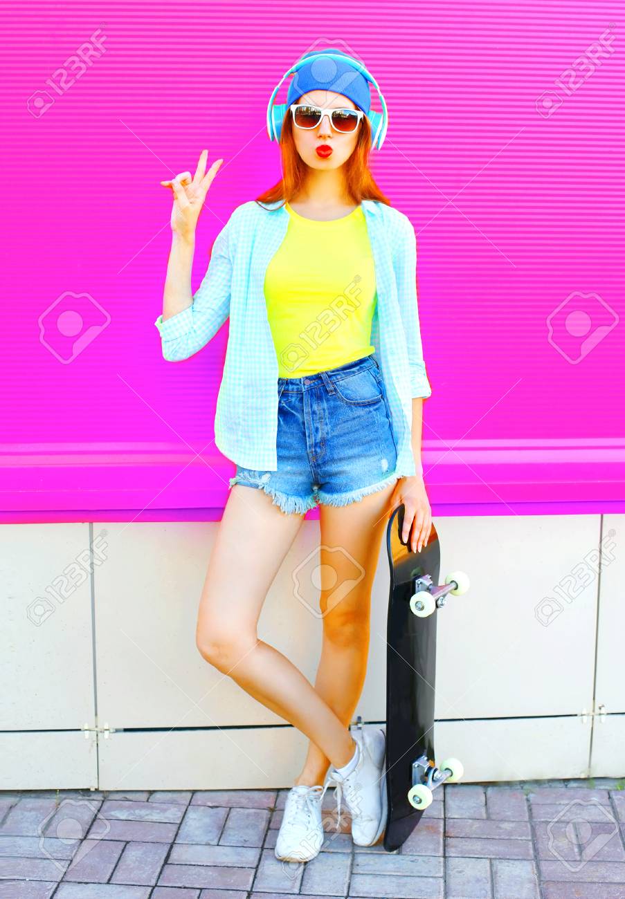 ファッションかわいい女性は カラフルなピンクの背景にスケートボードで音楽を聴きます の写真素材 画像素材 Image