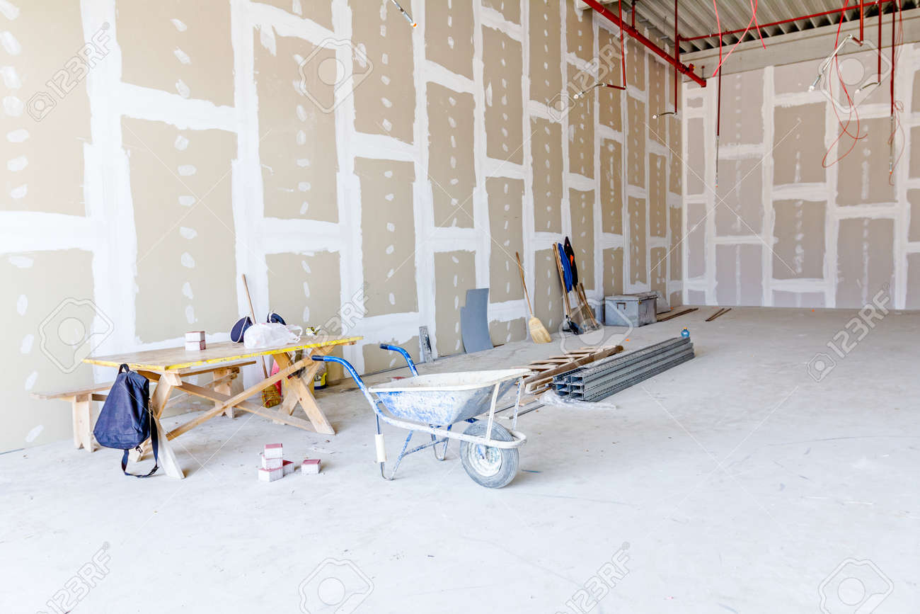Wheelbarrow is in front of tools for ground work. Thin square metal profiles for dry wall are stacked on ground in background. - 66202907 Wheelbarrow is in front of tools for ground work. Thin square metal profiles for dry wall are stacked on ground in background. - 66202907