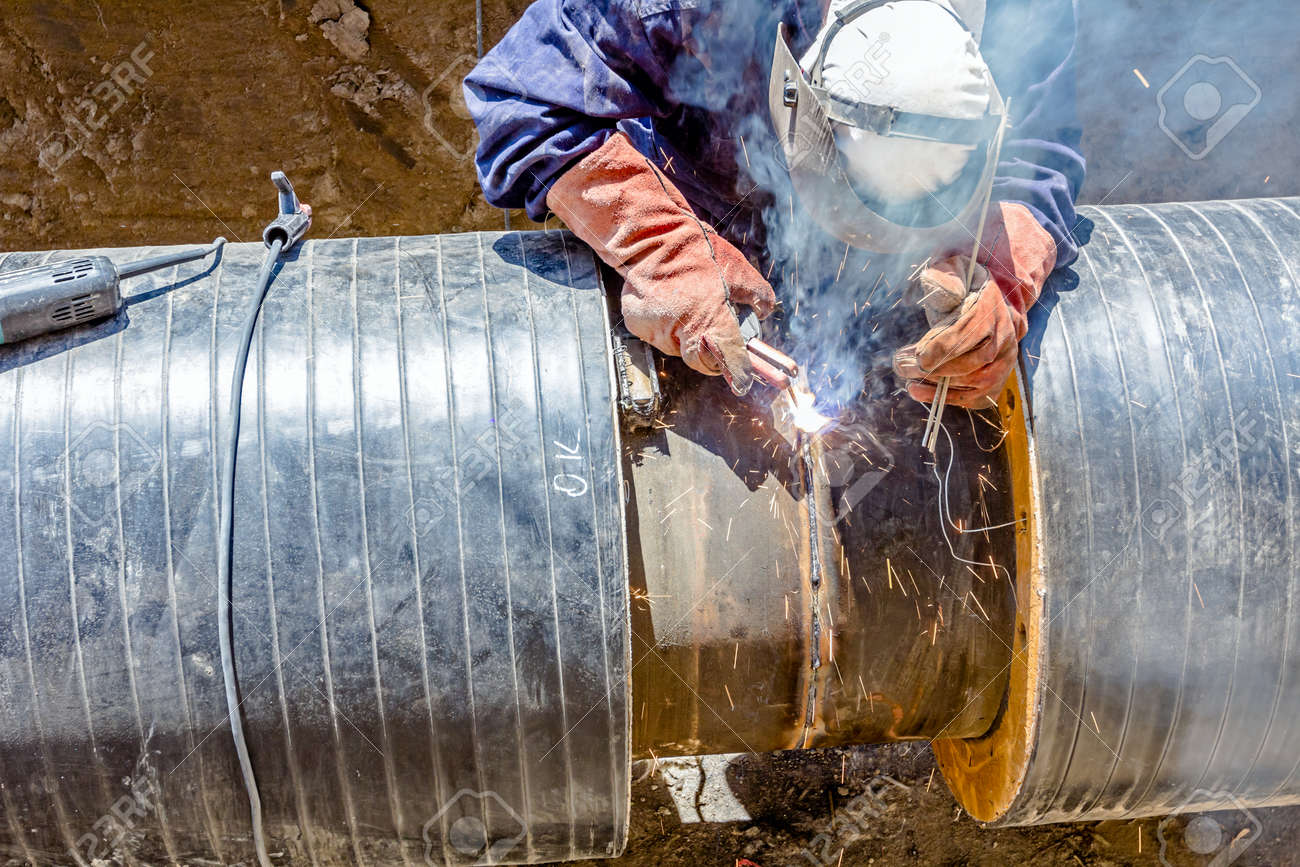 welder is in trench working hard arc welding pipeline welding pipe line