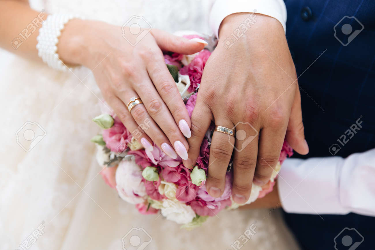 Close-up of the hands of the newlyweds with wedding rings, gently touch the wedding bouquet of peonies. - 110134072 Close-up of the hands of the newlyweds with wedding rings, gently touch the wedding bouquet of peonies. - 110134072