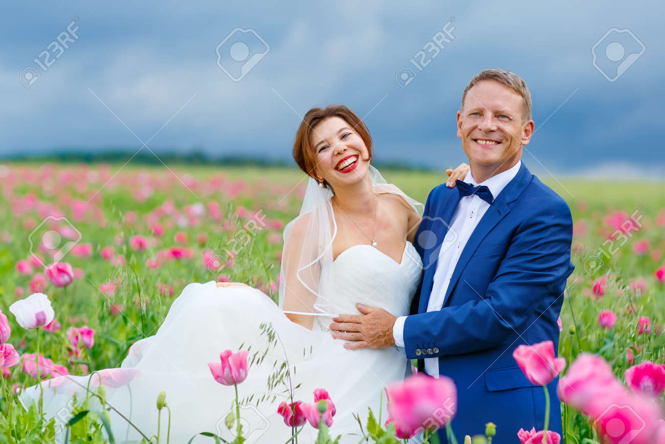 ピンクのポピー フィールドで幸せな結婚式です 美しい花嫁の白いドレスと新郎のキスをし 夏の日に花畑で楽しんで ちょうど結婚し 若い家族 の写真素材 画像素材 Image