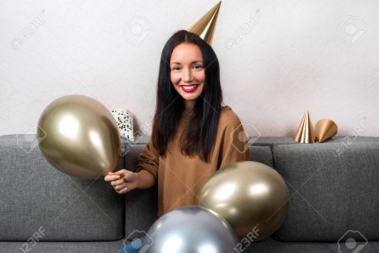 Smiling young woman wearing in party hat with balloons are celebrating birthday at home - 167848427 Smiling young woman wearing in party hat with balloons are celebrating birthday at home - 167848427