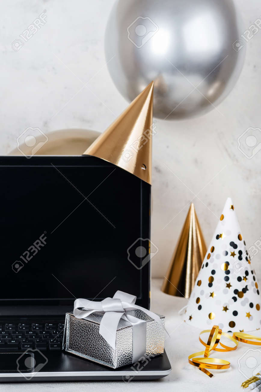 Silver festive box and blank screen laptop with party hats and balloons. - 167848535 Silver festive box and blank screen laptop with party hats and balloons. - 167848535