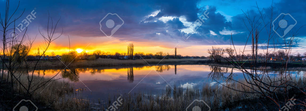 Beautiful golden sunset with reflection of clouds in the lake in the village panorama - 170818672 Beautiful golden sunset with reflection of clouds in the lake in the village panorama - 170818672