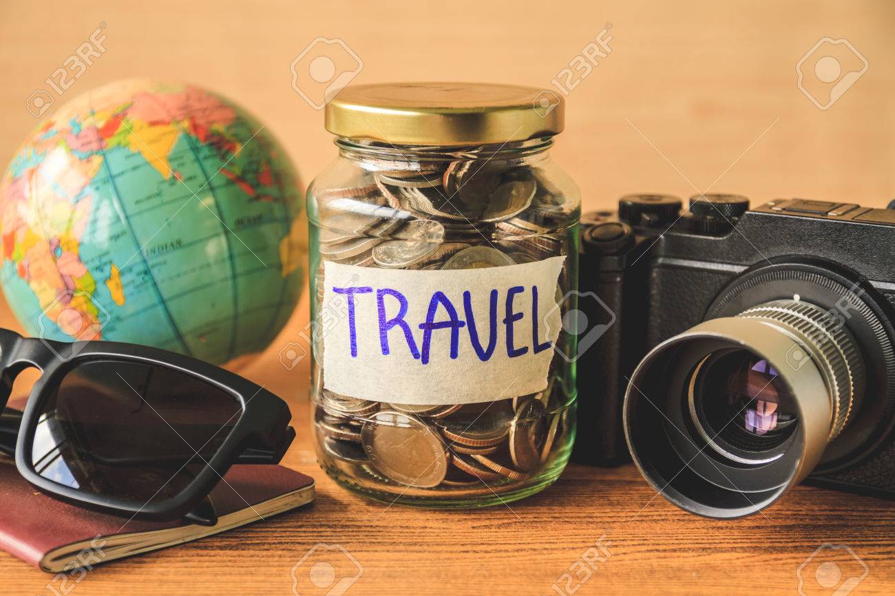 Coins in glass jar with accessories of traveler on wooden table. Saving money for travel concept - 75830392 Coins in glass jar with accessories of traveler on wooden table. Saving money for travel concept - 75830392
