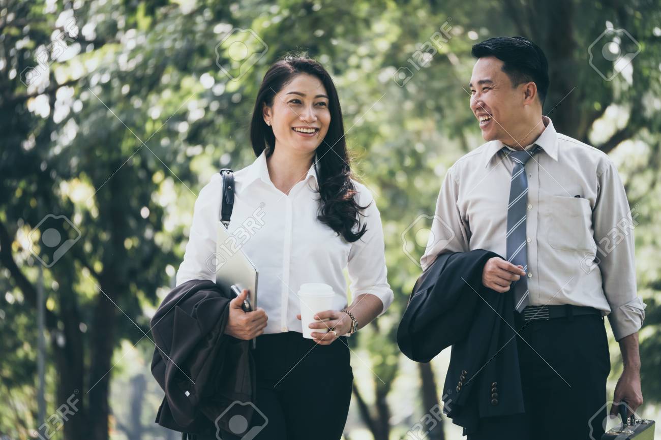 Happy Asian business man and woman walking and talking in the public park after finish work. - 92600961 Happy Asian business man and woman walking and talking in the public park after finish work. - 92600961