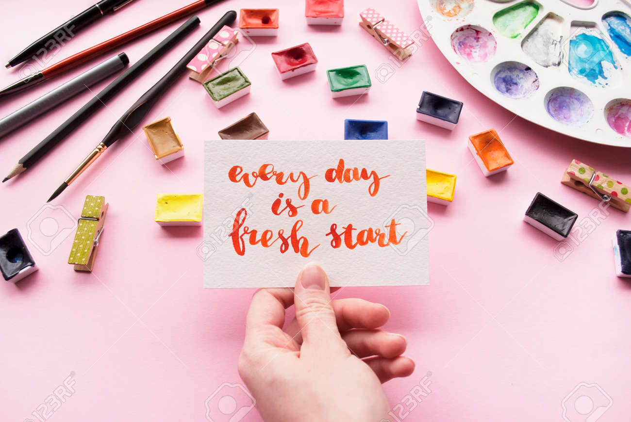 Filles Tenant Une Carte Avec Une Citation Inspirante Chaque Jour Est Un Nouveau Depart Ecrit Dans Un Style Calligraphique Espace De Travail De L Artiste Sur Fond Rose Pose A Plat Banque D Images