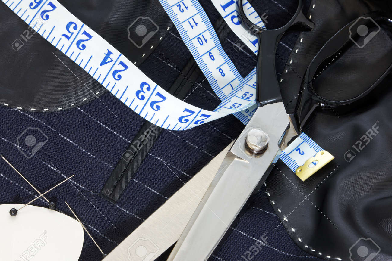 Still life photo of the inside of a bespoke suit jacket with hand stitching and scissors, tape measure, chalk and pins. - 12382312 Still life photo of the inside of a bespoke suit jacket with hand stitching and scissors, tape measure, chalk and pins. - 12382312
