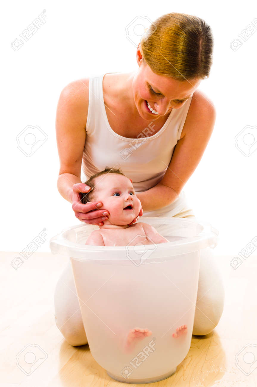 Mere Adulte Portant Des Vetements Decontractes Vives Elle S Agenouille Sur Le Sol Et Baigne Son Bebe Nouveau Ne Dans Le Seau De Bain Avec Precaution Elle Garde La Tete Du Bebe Isole Sur