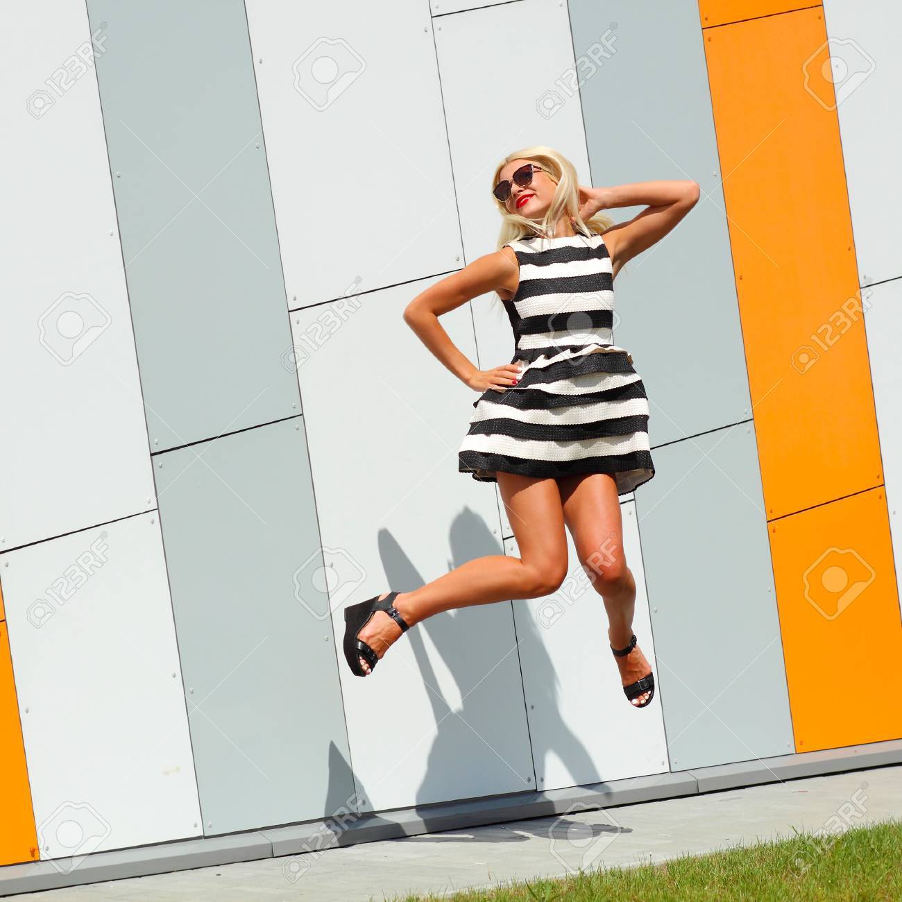 トレンディなおしゃれな女の子は感情的にオレンジ色の壁の背景色の上でジャンプ の写真素材 画像素材 Image