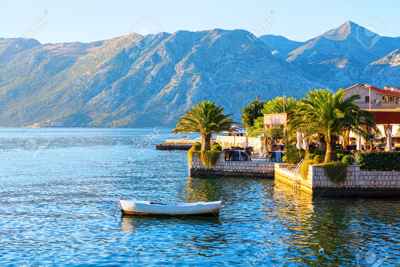 Coastal restaurant terrace at the tropical beach . Cafe terrace overlooking the Kotor Bay in Montenegro . Moored white boat - 169400074 Coastal restaurant terrace at the tropical beach . Cafe terrace overlooking the Kotor Bay in Montenegro . Moored white boat - 169400074