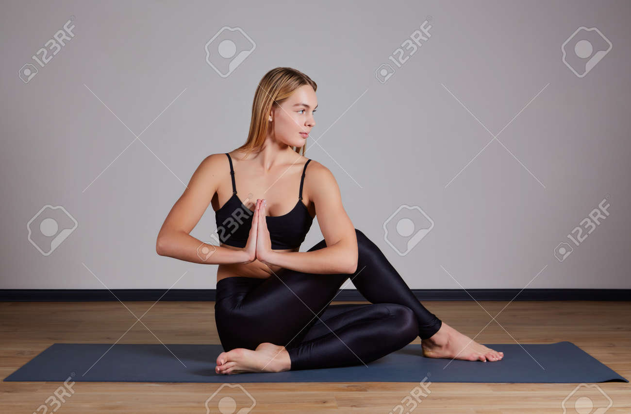 Young attractive woman practicing yoga, doing Half lord of the fishes exercise, Ardha Matsyendrasana pose with namaste. Working out, wearing sportswear, pants and top, indoor full length, yoga studio - 169021138 Young attractive woman practicing yoga, doing Half lord of the fishes exercise, Ardha Matsyendrasana pose with namaste. Working out, wearing sportswear, pants and top, indoor full length, yoga studio - 169021138