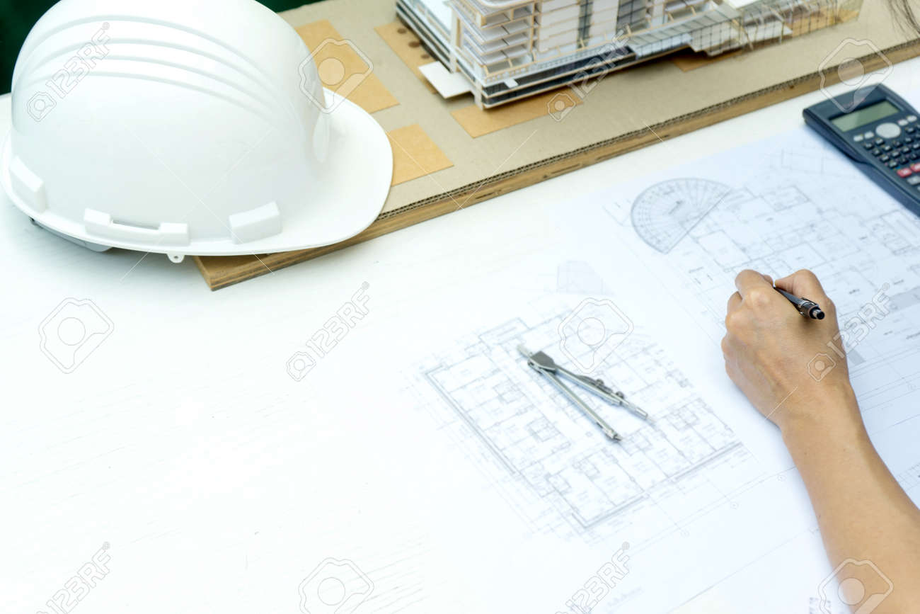 architects or engineer holding pen pointing equipment architects On the desk with a blueprint in the office building model and hat are on the table. - 169322411 architects or engineer holding pen pointing equipment architects On the desk with a blueprint in the office building model and hat are on the table. - 169322411