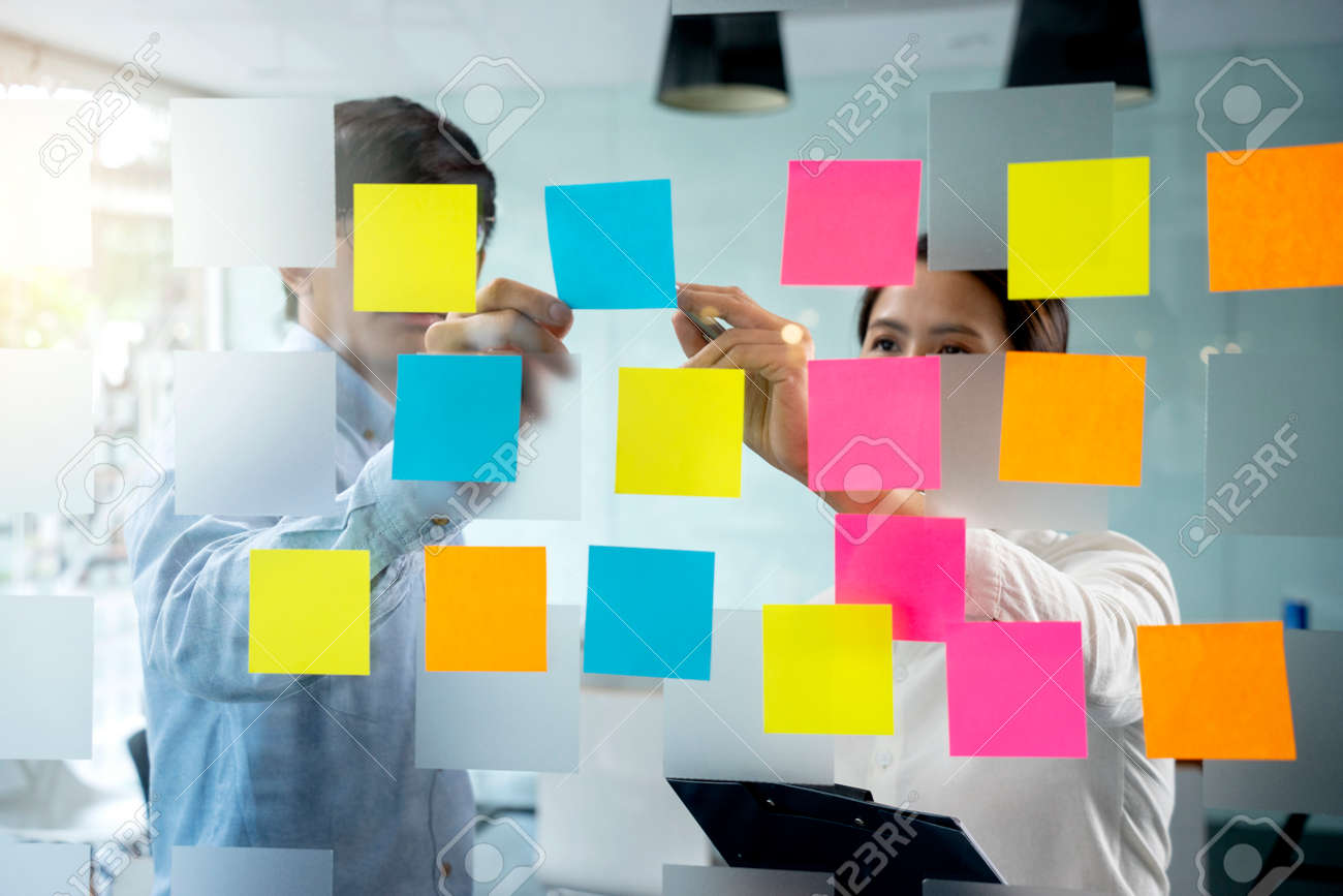 Businessmen and woman are standing He giving advice and brainstorming for Find an ideal and Write to notepad and stick it on the board. - 169232045 Businessmen and woman are standing He giving advice and brainstorming for Find an ideal and Write to notepad and stick it on the board. - 169232045
