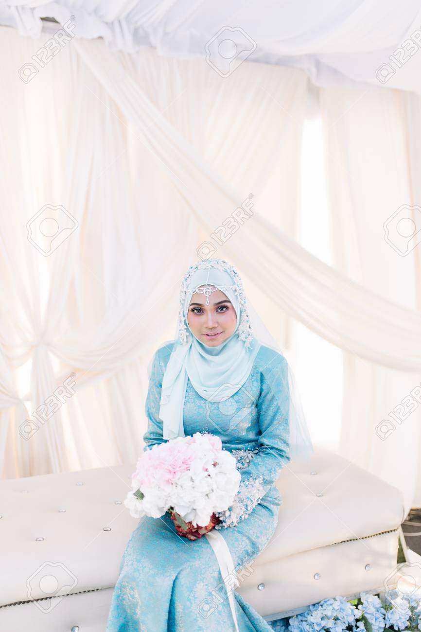 Portrait of Malaysian Muslim woman in wedding dress sitting and..