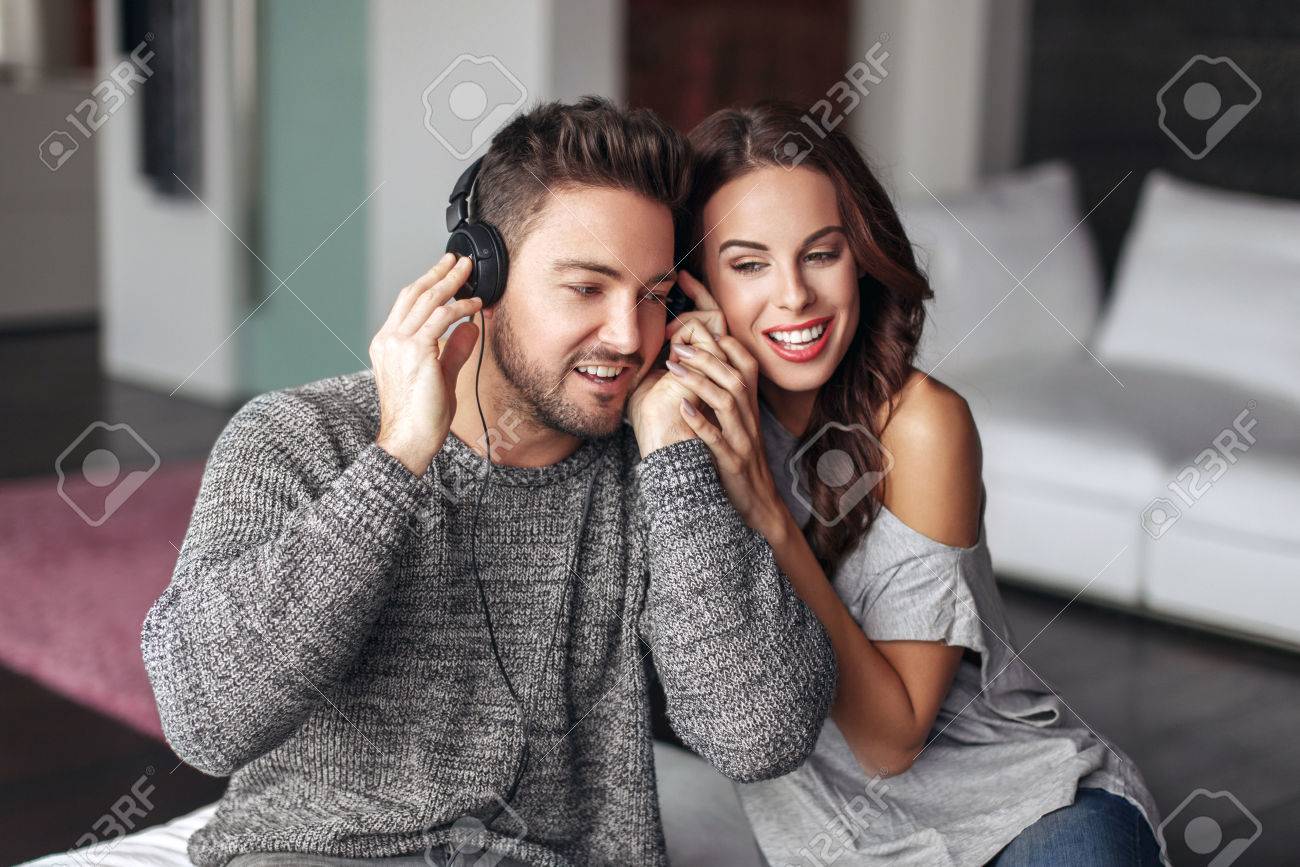 Happy young couple listening music and at home, sharing headphones - 58295721 Happy young couple listening music and at home, sharing headphones - 58295721