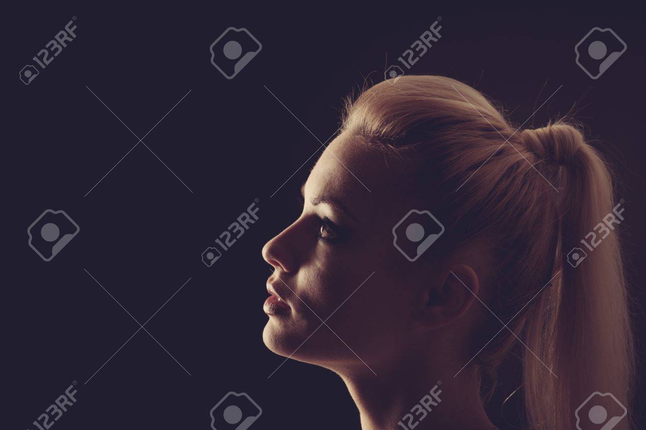 彼女の顔は 黒の背景上で物思いにふける影絵に柔らかな光と闇の中で美しい金髪女性の肖像画 の写真素材 画像素材 Image